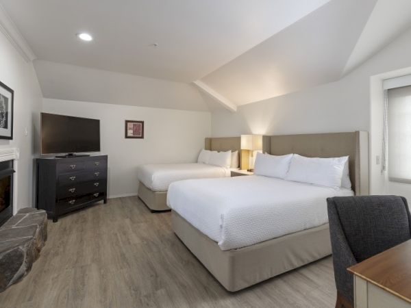 A spacious hotel room with two queen beds, a dresser, a flat-screen TV, desk chair, and a fireplace in a bright, modern setup. End with a period.