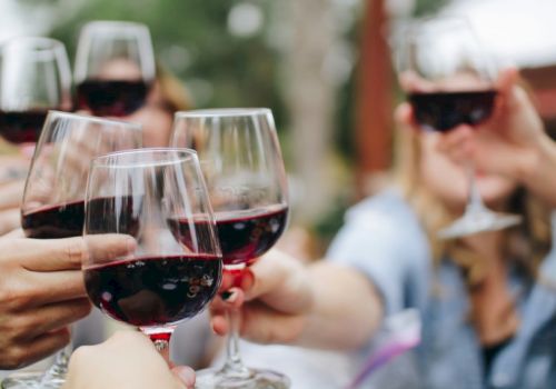 A group of people toasting with glasses of red wine in a cheerful outdoor setting, clinking glasses as they celebrate.