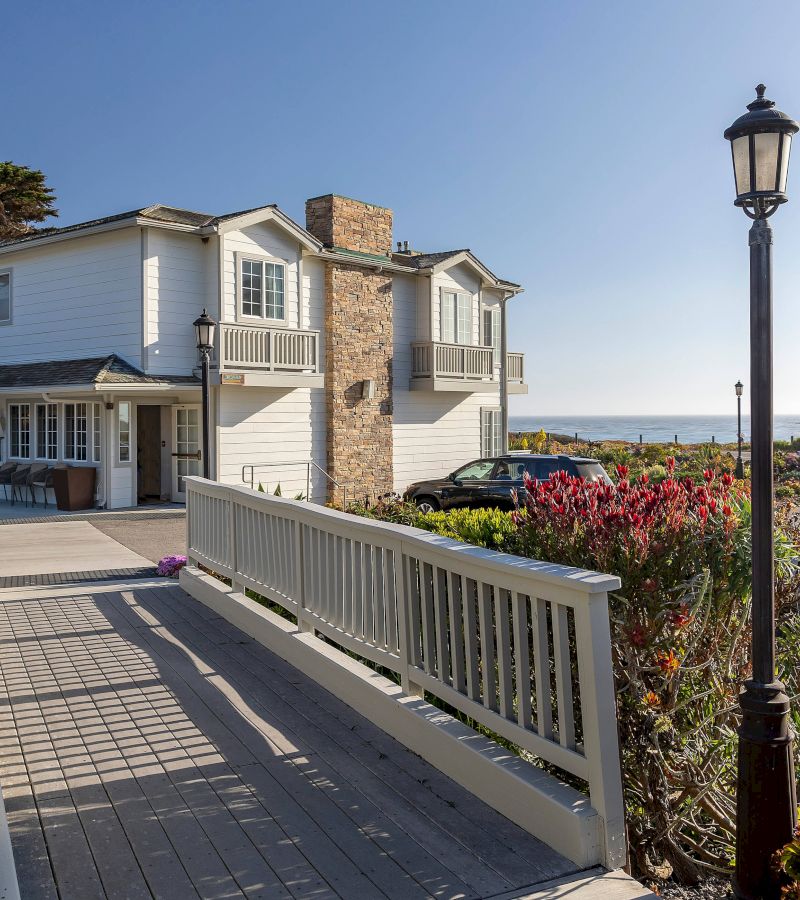 A white building with a stone chimney and balcony overlooking the ocean.