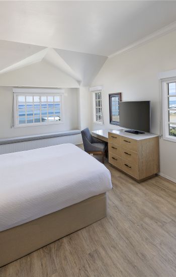 A wide-angle view of a room with a bed, desk, TV, and window.